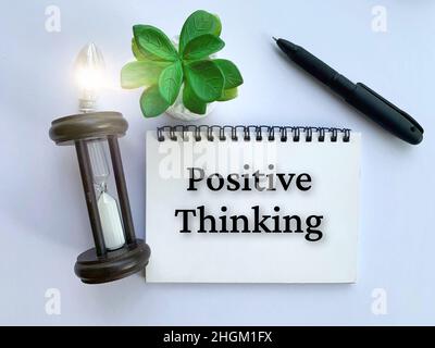 Top view of Positive Thinking on notebook with shining bulb, pen, hourly glass and plant background. Business concept. Stock Photo