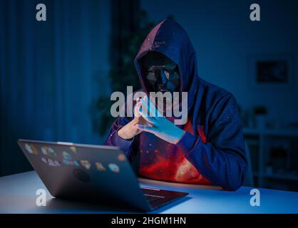 Hacker in mask work on laptop Stock Photo