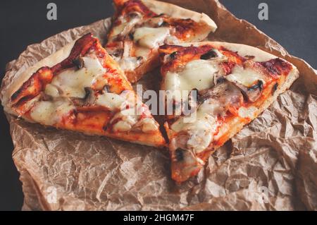 slices of freshly baked pizza on a black serving chalkboard on a dark background Stock Photo