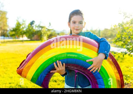 beautiful latin hispanic seven years old girl with big rainbow balloon outdoors in summer park Stock Photo