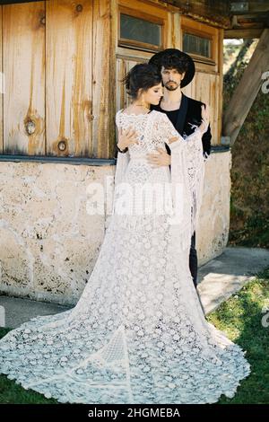 Groom hugs bride near the wall of a wooden house Stock Photo