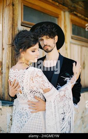 Groom hugs bride near the wall of a house. Close-up Stock Photo