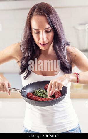 Brunette nibbes on freshly baked sausage in a pan with rosemary leaves. Stock Photo