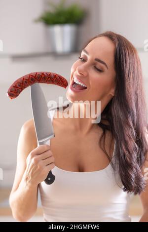 Woman is about to bite from grilled sausage stabbed on a big knife. Stock Photo