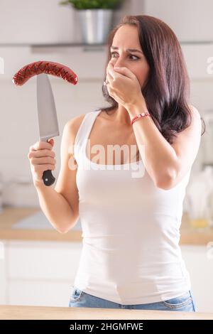 Woman resist grilled sausage on top of knife in her hand. Stock Photo