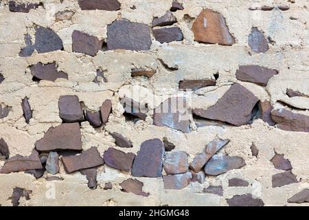 Photograph of an old and deteriorating wall manufactured with grey concrete that is cracking and brown irregular shaped stones Stock Photo
