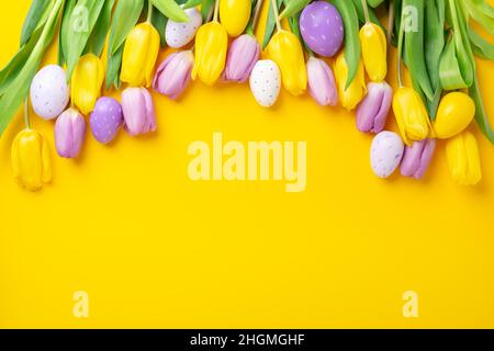 Easter greeting card. Multicolored easter eggs and tulips on yellow background. Easter concept Stock Photo