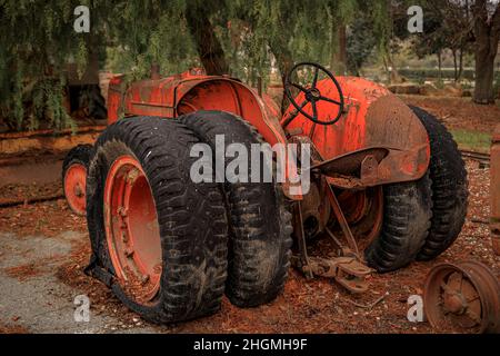 Old and rusty abandoned heavy equipment, a tractor amongst trees with fallen yellow leaves on the ground Stock Photo