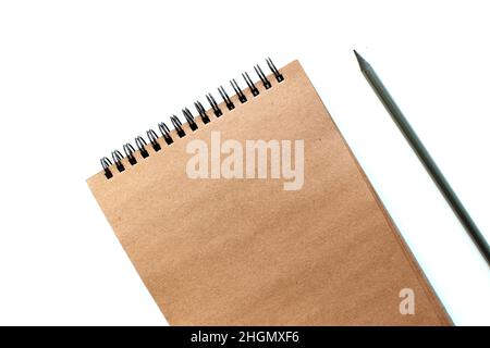 Top view of closed spiral blank craft paper cover notebook with pencil on white desk background. Stock Photo