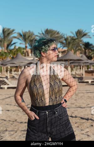 Young woman with blue green hair on the sand on the beach in the shadows from the grid.  Stock Photo