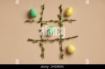 Easter eggs in a frame made of spring branches on a beige background. Tic-tac-toe game. Easter theme flatlay. Stock Photo