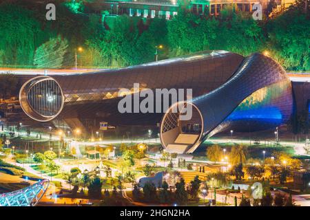 Tbilisi, Georgia. Evening Night Scenic Aerial View Of Concert Music Theatre Exhibition Hall In Summer Rike Park Tbilisi, Georgia. Bright Night Street Stock Photo