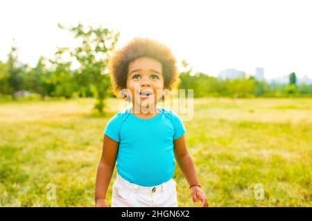 adorable small mixed race girl walking alone in park at sunset time Stock Photo