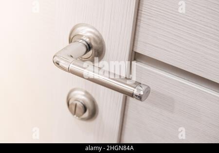 Metallic chrome handle on white wooden interior door. Modern door handle. Stock Photo