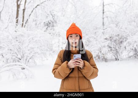 Beautiful asian woman walking in the park, uses the phone for online shopping, on a winter snowy day Stock Photo