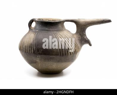 Spouted pitcher ca. 1050-800 B.C. Iran This pitcher has a squat, globular body, a flat base, a wide neck and a flaring rim. A small handle connects the rim and neck on one side; on the other a spout rises vertically from the body of the pitcher before extending outward horizontally. The spout is attached to the rim by a small bridge. A drooping point protrudes from the spout where it emerges from the body. The pitcher is made of burnished grey clay and decorated with oblique fluting. It was made on a potter’s wheel, perhaps in two halves, with the spout and handle added later.This pitcher was Stock Photo
