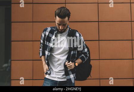 Trendy dressed male student with backpack looking down during leisure time in city, Stock Photo