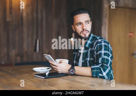 Caucaisan male blogger using smartphone application during coffee time in cafe interior Stock Photo