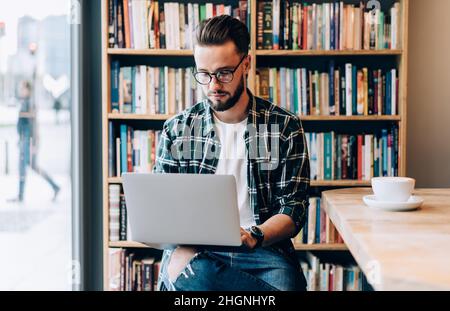 hipster guy in spectacles searching education information via netbook in library Stock Photo
