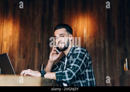 Cheerful man making positive cell conversation during distance job in coworking space,  Stock Photo