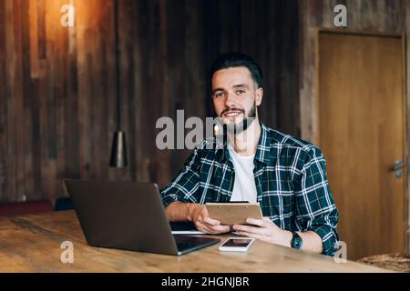 happy hipster guy working remotely in cafe interior sitting at desk with tech netbook Stock Photo