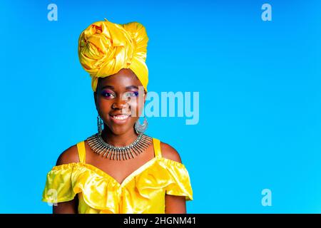 African woman with yellow silk turban and silver earrings and nose piercing in blue studio background Stock Photo