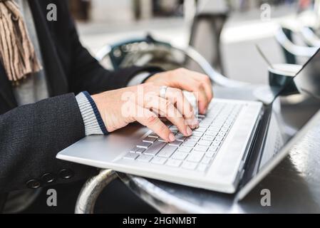 Unrecognizable man typing and browsing data on laptop while sitting at table and working remotely in street cafeteria Stock Photo
