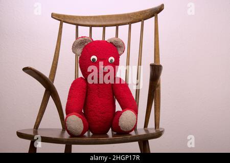 red teddy bear sitting on a wooden chair with a plain background Stock Photo