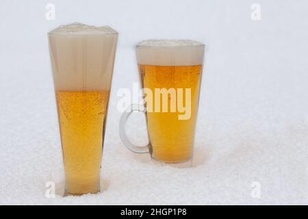 Two glasses of light beer with foam in the snow. Cold beer during winter. Stock Photo
