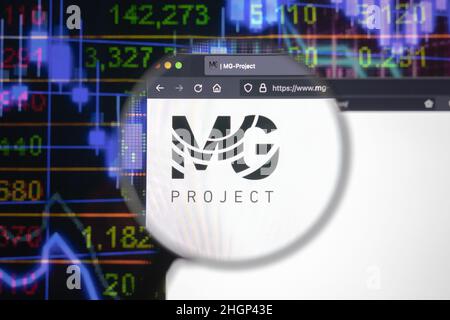 MG Project company logo on a website with blurry stock market developments in the background, seen on a computer screen through a magnifying glass. Stock Photo