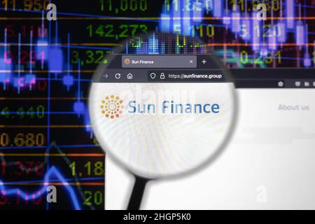Sun Finance company logo on a website with blurry stock market developments in the background, seen on a computer screen through a magnifying glass. Stock Photo