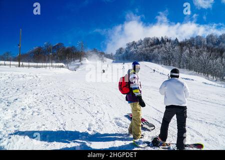 Two snowboarders snowboarding in mountain. Snowboarders enjoying leisure activities on outdoors. Group of friends enjoying the winter season. Stock Photo