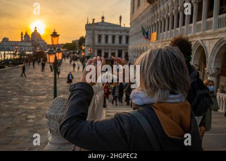 Woman with iPhone at sunset with the lamp standards on the Rive Shiavoni, The Grand Canal, Venice, Italy Stock Photo