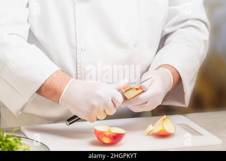 Unrecognizable chef in uniform cutting an apple on a plastic cutting board Stock Photo