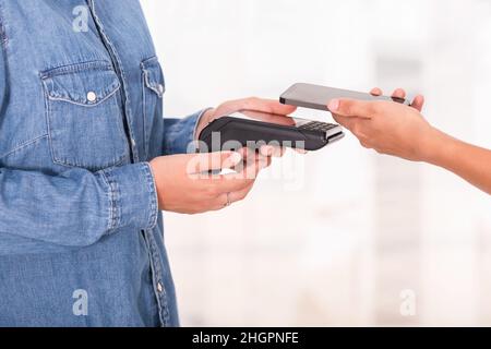 Close up of unrecognizable person making contactless payment holding mobile phone to reader Stock Photo