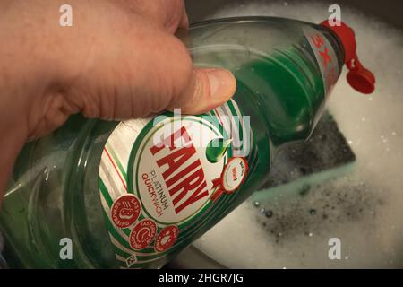 Norwich, Norfolk, UK – January 2022. Unidentifiable male using Fairy Platinum quick wash detergent to wash the dishes Stock Photo