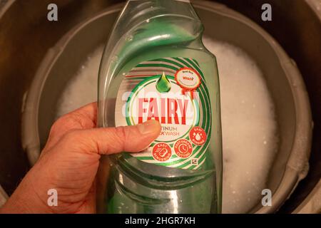 Norwich, Norfolk, UK – January 2022. Unidentifiable male using Fairy Platinum quick wash detergent to wash the dishes Stock Photo