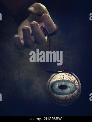 Fine art depicting a hand dangling an eyeball on a red string like a puppet Stock Photo