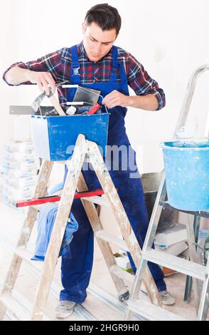 Young concentrated builder handyman choosing tool in toolbox Stock Photo