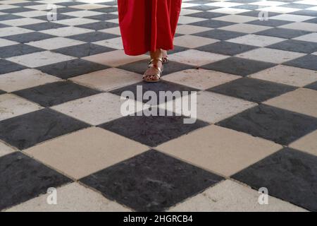 Close up of a woman in red dress and elegant sandals walking on a checkered marble black and white floor Stock Photo
