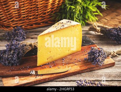 Triangle slice of cheese with buds of lavender on wooden cutting board Stock Photo