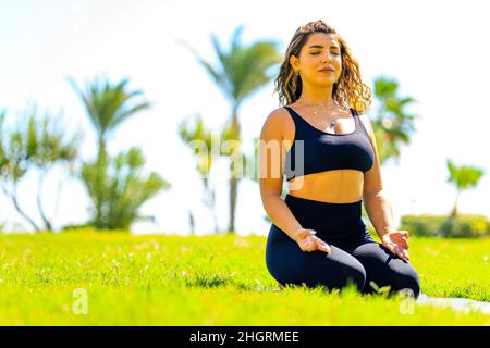 Young indian attractive woman practicing yoga , deep calm breathing outdoors in summer green park Stock Photo