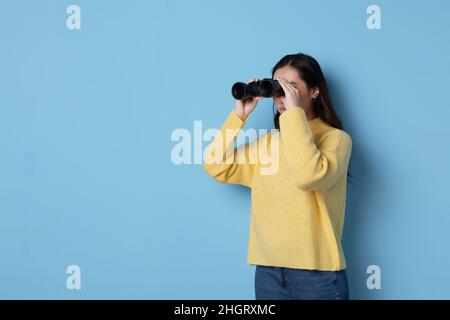 Studio photo with blue background of an asian woman looking through binoculars Stock Photo