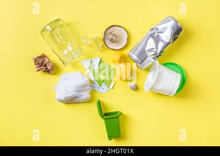 Clean trash to recycle in small bin metal, plastic paper and glass. Recycling concept on yellow. Stock Photo