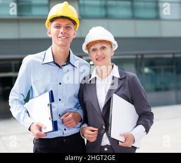 Female designer and her partner are standing with laptop and folder Stock Photo
