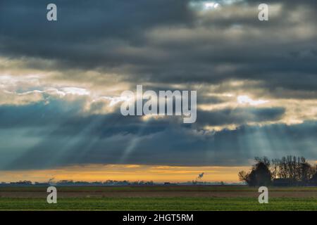 Sun rays through dark clouds above a Dutch farm. Farm and fields in the Dutch province of Groningen under a dramatic sky at sunset Stock Photo