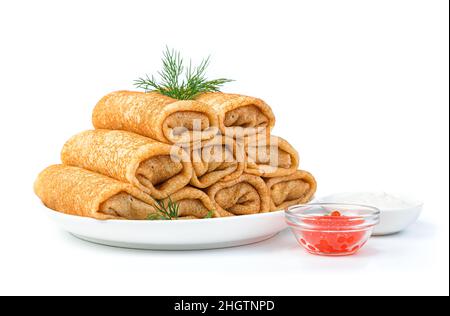 A stack of thin stuffed pancakes in a white plate with dill, sour cream and red caviar. Side view, close-up. Stock Photo