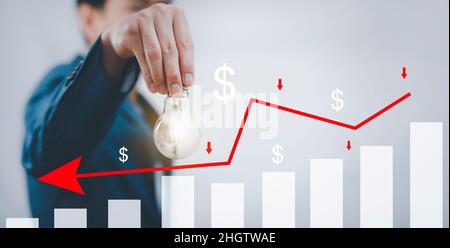 Businessman holding light bulb with losses on the stock market chart concept, market chart and Red arrows fall to the ground, indicating the economic Stock Photo