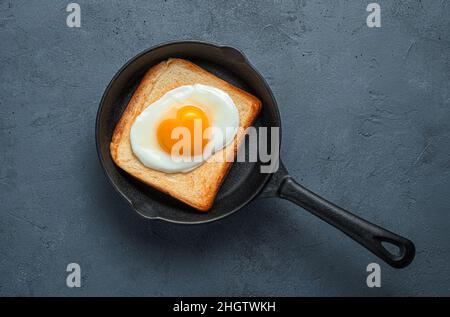 Fried eggs with a heart-shaped yolk on toast in a frying pan. Top view, copy space. Stock Photo