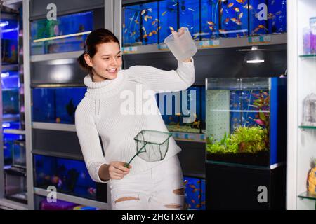 Girl with net and water container is going to catch juvenile fish from aquarium Stock Photo